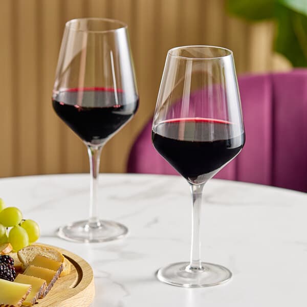 Two Acopa Silhouette wine glasses filled with red wine on a table.