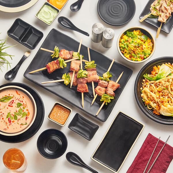 A table with Acopa Ugoki matte black plates with ivory rims, a bowl of rice and vegetables, and a bowl of soup on it.