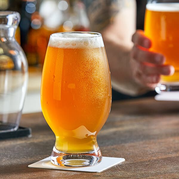 An Acopa Select craft beer glass full of beer on a bar counter.