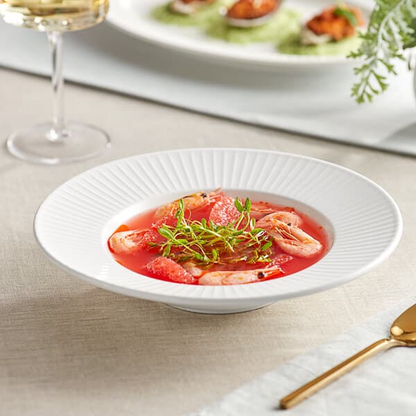 A bowl of Acopa Cordelia bright white porcelain soup with shrimp and herbs.
