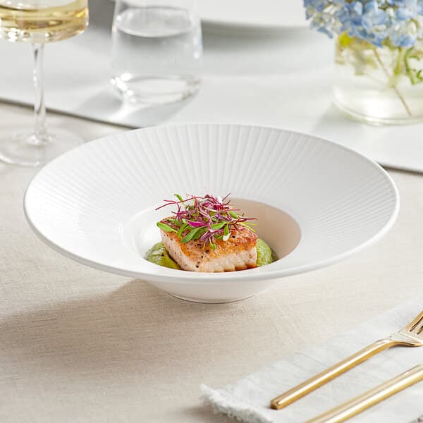 An Acopa Cordelia white porcelain bowl with a plate of food on a table.