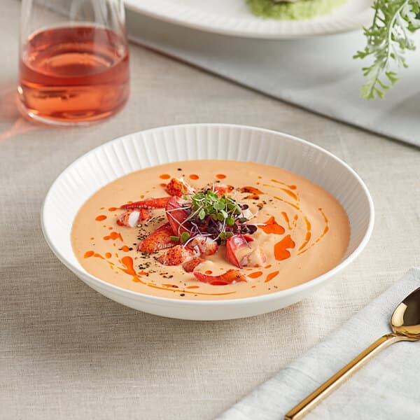 A bowl of soup with fruit and sprouts in an Acopa Cordelia porcelain bowl with a spoon.