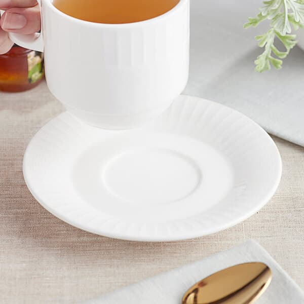 A hand holding a cup of tea on a white Acopa Cordelia saucer.