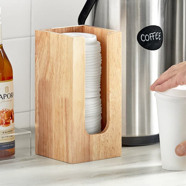 A hand holding a cup of coffee next to a wooden Acopa coffee cup holder.