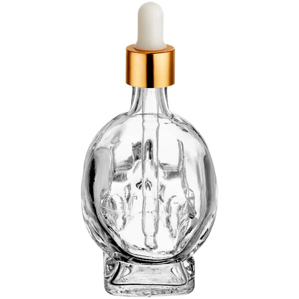 An Acopa clear glass skull bitters bottle with a gold cap.