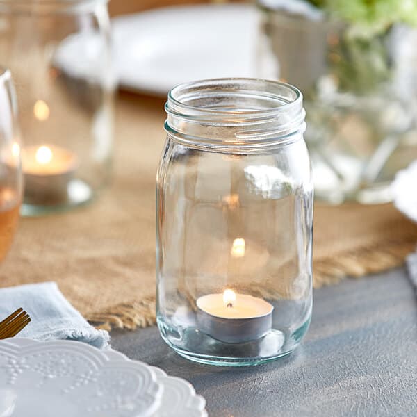 A glass jar with a candle inside on a table.