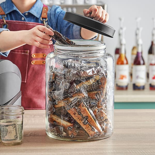 A person putting food into a glass jar with a black metal lid.