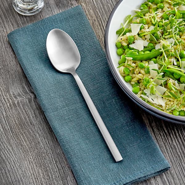 An Acopa Phoenix stainless steel spoon on a napkin next to a bowl of rice and peas.