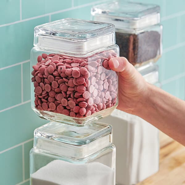 A hand holding a clear Acopa glass jar full of pink candies.