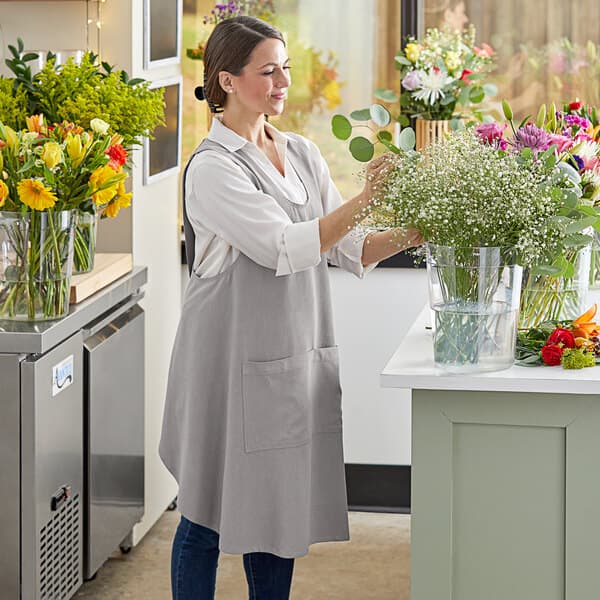 A woman in an Acopa Ashville linen smock bib apron arranging flowers in a vase.