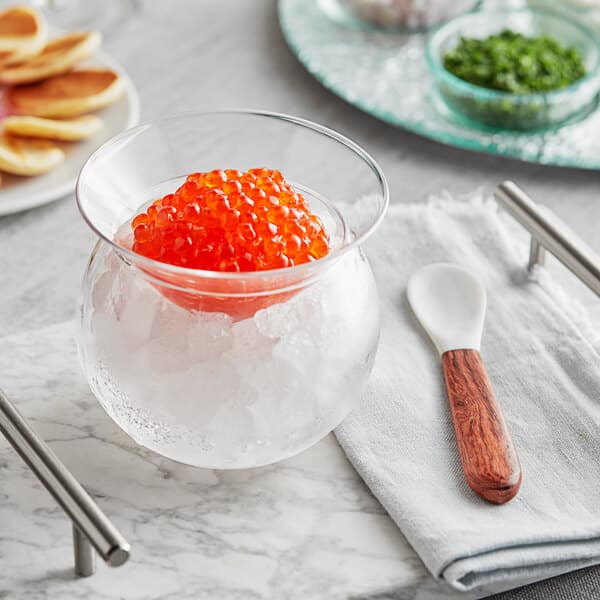 A bowl of red caviar with a spoon and a server on a table.