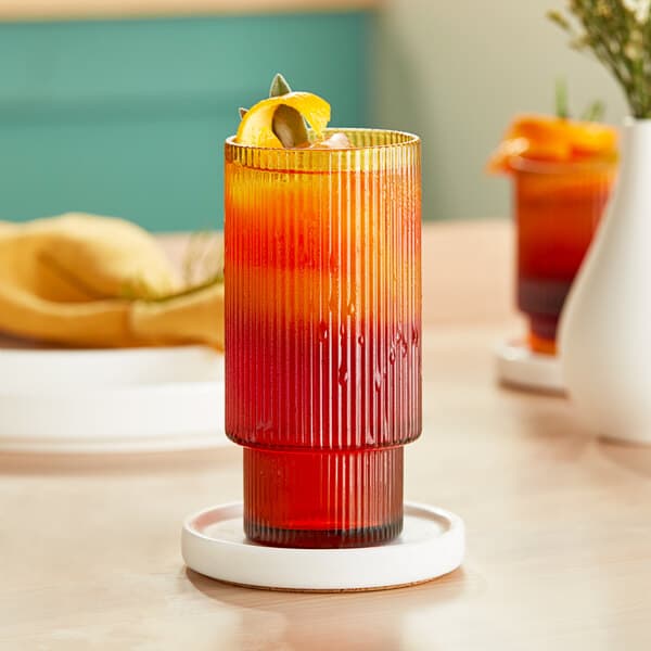 An Acopa amber highball glass filled with orange juice and a slice of orange on a table.