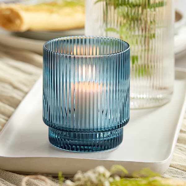 An Acopa Lore blue glass tealight holder with a lit candle on a white tray.