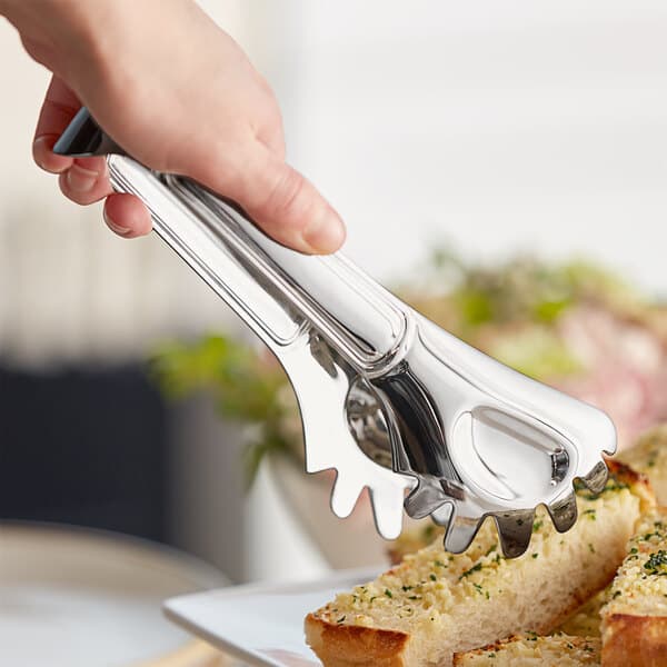 A hand using a metal Acopa bread tong to pick up a piece of bread.