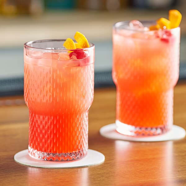 Two Acopa Rivulet stackable beverage glasses of red liquid with orange slices on a table.