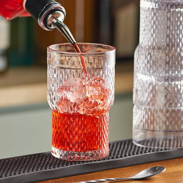 A person pouring a red drink from a bottle into an Acopa Rivulet beverage glass on a table.