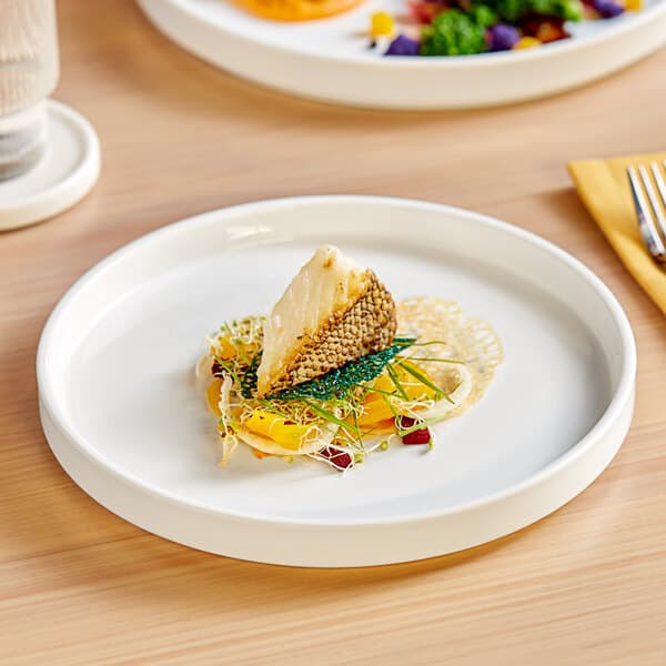 A piece of fish on an Acopa Lore porcelain plate with a raised rim.