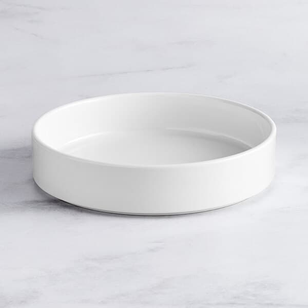 An Acopa Lore bright white porcelain deep plate with a raised rim on a white table.