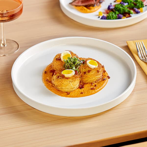 An Acopa Lore bright white porcelain plate with a small dish of food on it.