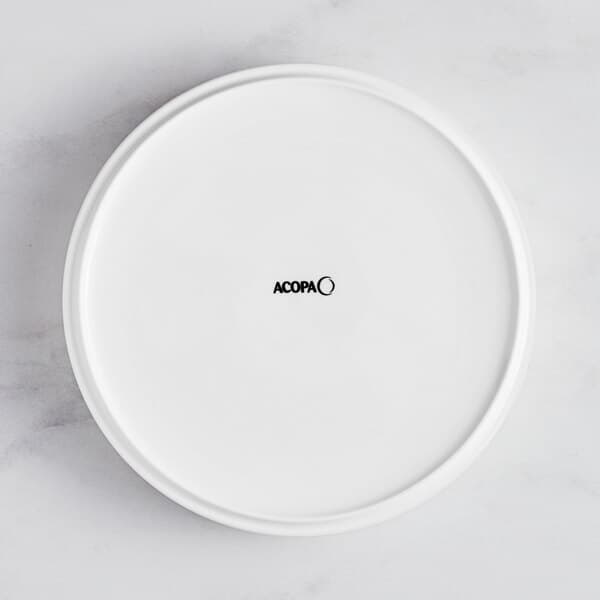 A bright white Acopa Lore porcelain plate with a raised rim and black text that says "oca" in the center.