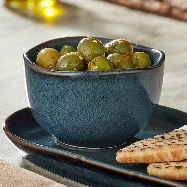 An Acopa Highlands skyfall blue bouillon cup filled with green olives and crackers.