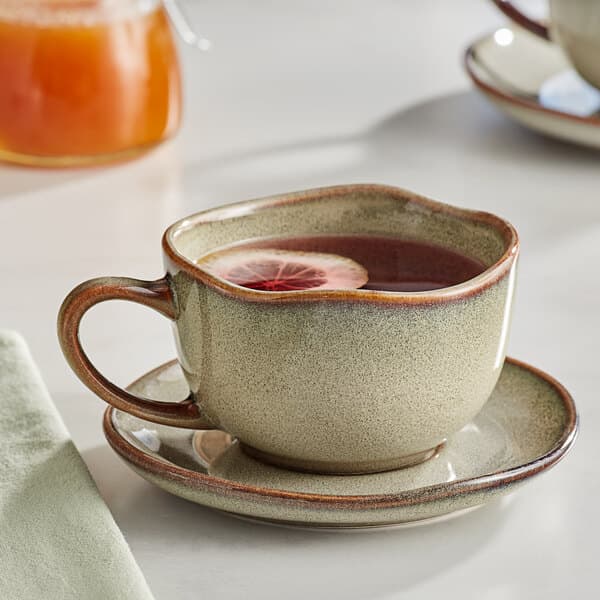 An Acopa Highlands heather gray china cup of tea with a lemon slice on a saucer.