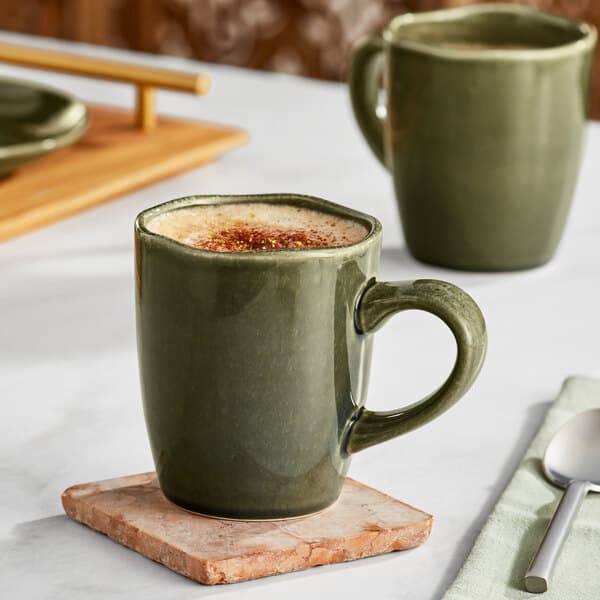 Two juniper green Acopa china mugs filled with coffee on a marble table.