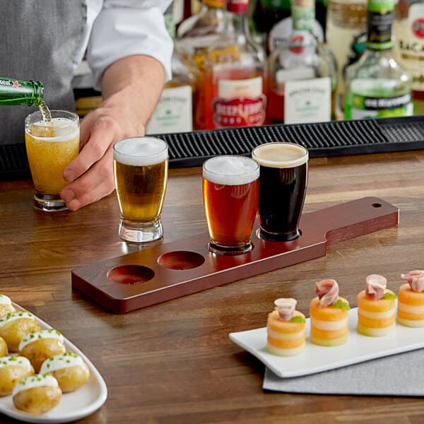 An Acopa mahogany flight paddle holding glasses of beer on a table in a cocktail bar.