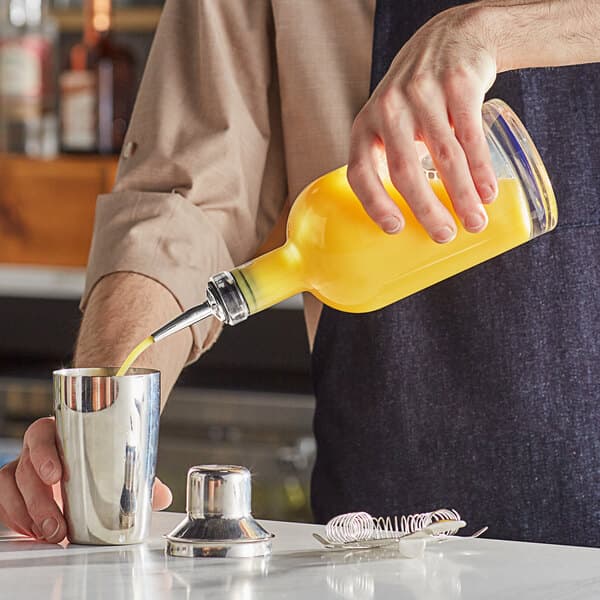 A person holding an Acopa clear glass bottle and pouring a drink into a cup.