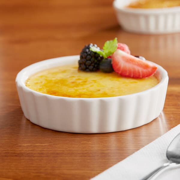 A white Acopa fluted porcelain bowl filled with creme brulee and fruit on a table.