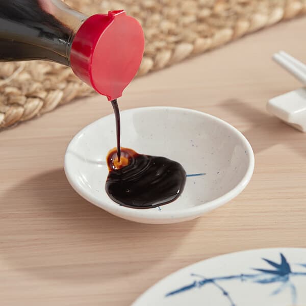 A person pouring sauce into a bowl on a table using an Acopa Biru sauce dish.