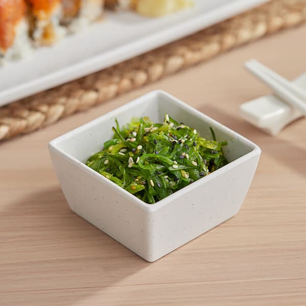 A white Acopa Biru melamine bowl filled with green seaweed salad on a table.
