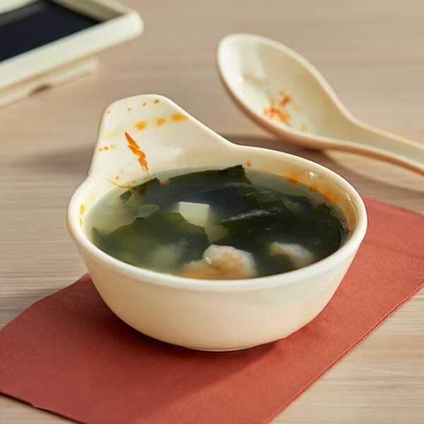 An Acopa Brassia melamine dip bowl filled with soup with a spoon next to it.