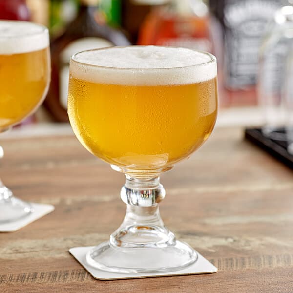 Two Acopa schooner glasses filled with beer on a wooden table.