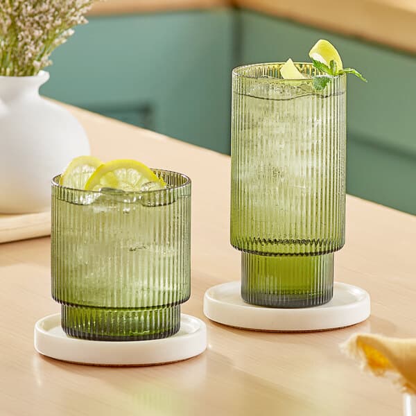 Two Acopa Lore green glasses with drinks and lemons on a table.