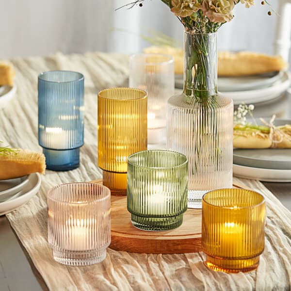 A group of Acopa Lore green glass tealight holders with candles on a table with flowers.