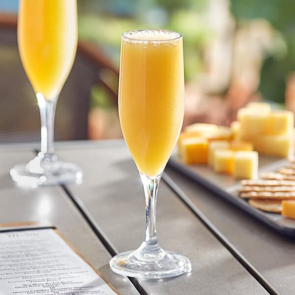 A table with two Acopa Endure Tritan plastic champagne flutes filled with orange juice, with cheese and crackers.