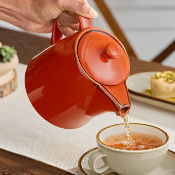 A person pouring tea into an Acopa Sedona Orange teapot.