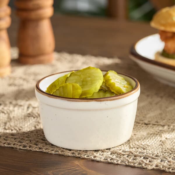 A bowl of pickles on a table with a sandwich.