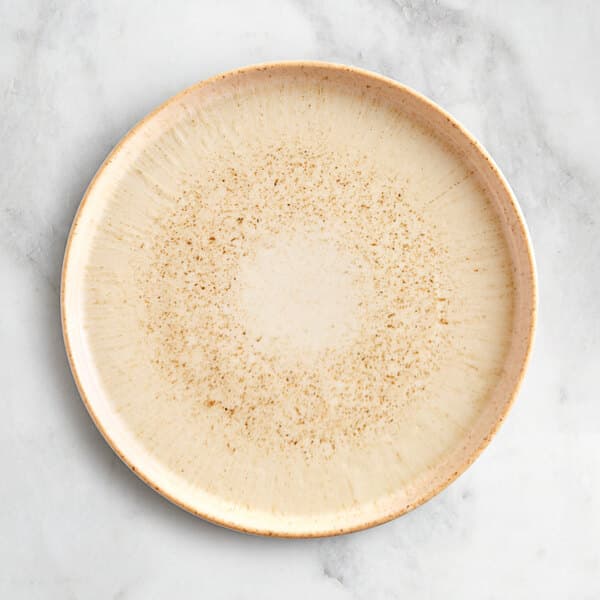An Acopa Cape beige porcelain plate with brown specks on a white surface.