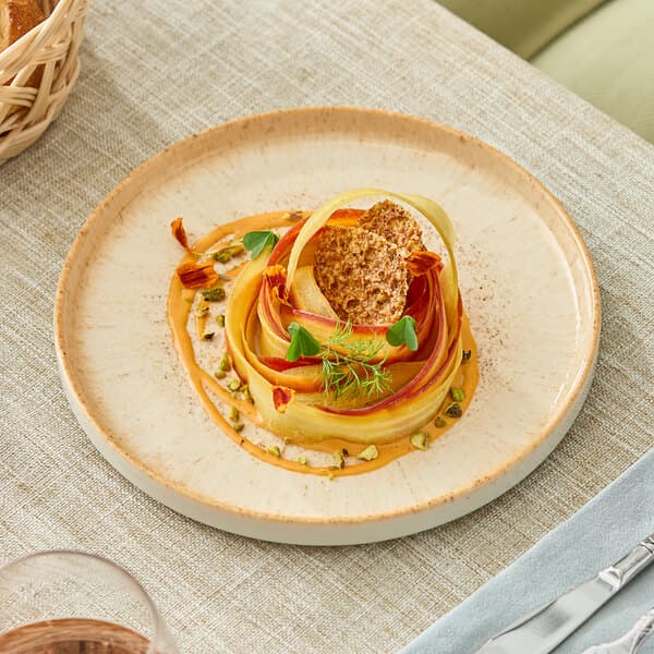 A round beige porcelain plate with a slightly raised rim, shown with a gourmet food presentation.