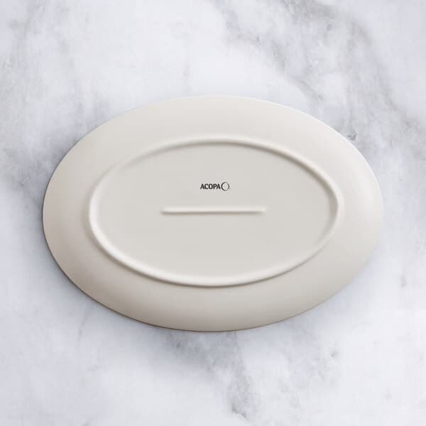 An Acopa Cape white porcelain oval platter with a white rim on a marble surface.