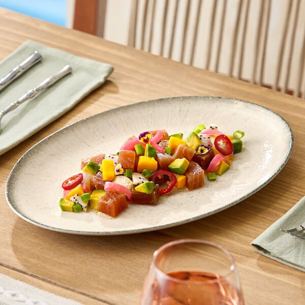 An oval gray porcelain platter displaying a colorful arrangement of diced vegetables and fish.