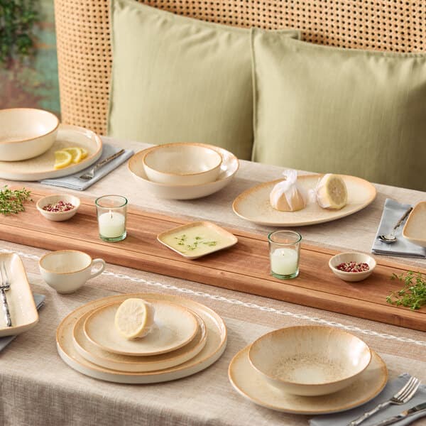 An oval beige porcelain platter displayed on a dining table set with matching dinnerware and decor.