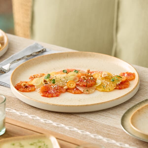 A round beige porcelain plate with a slightly raised rim, shown on a table setting.