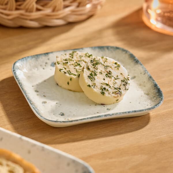 A square gray porcelain butter dish holding two rounds of herb butter.