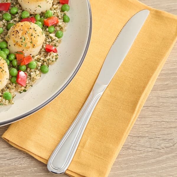 An Acopa stainless steel table knife on a plate of scallops, peas, and rice.
