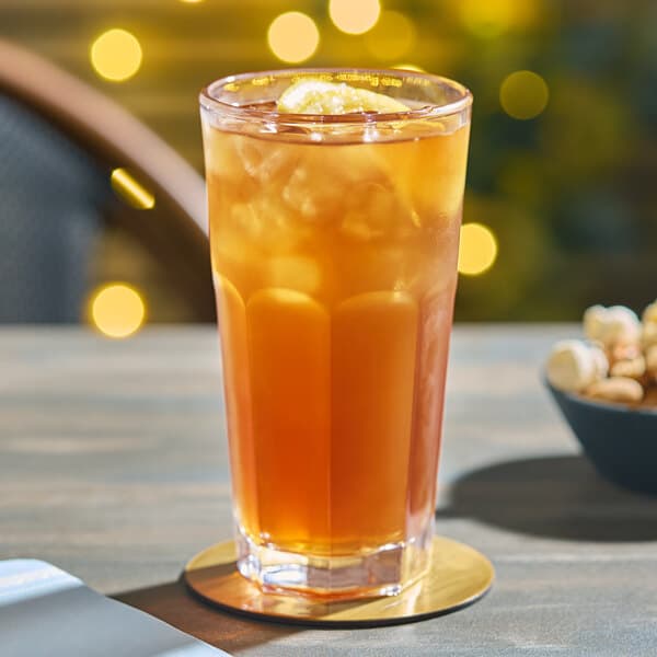 An Acopa Memphis cooler glass of orange liquid with ice on a table.