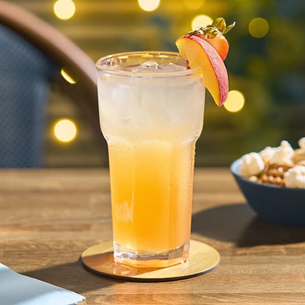 An Acopa Memphis highball glass of orange liquid with a fruit on the rim on a table.