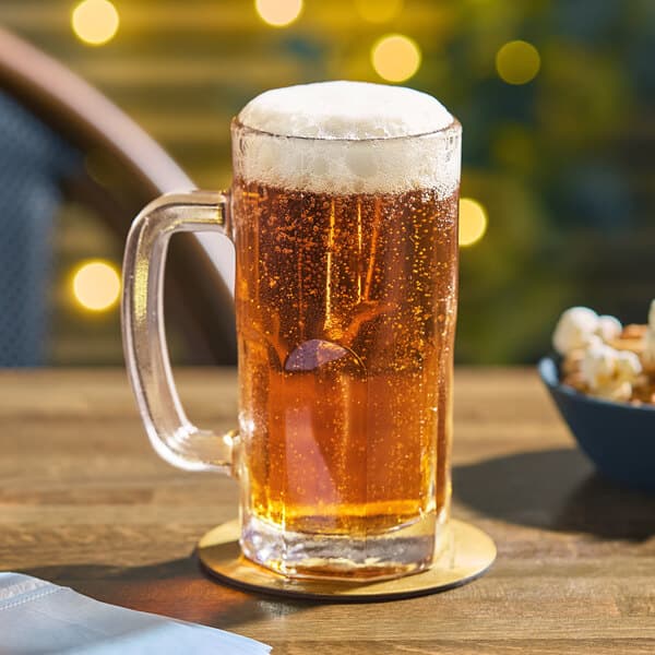 An Acopa beer mug filled with beer on a table with a bowl of popcorn.